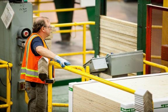 An operator at the controls beside a wood-panel production line.