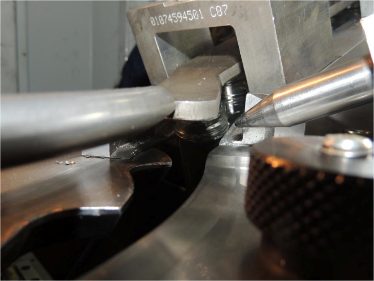 A plastic preform jammed in the guide rail beside the metal plunger.